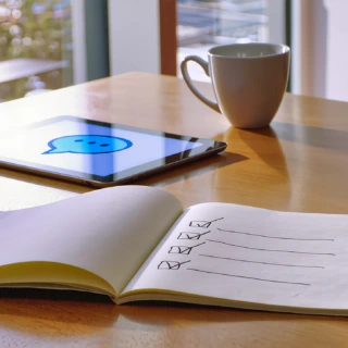 Fünf KI-Mythen im Faktencheck: Notizbuch mit Häkchen-Liste neben Tablet mit Chat-Symbol auf hellem Schreibtisch.